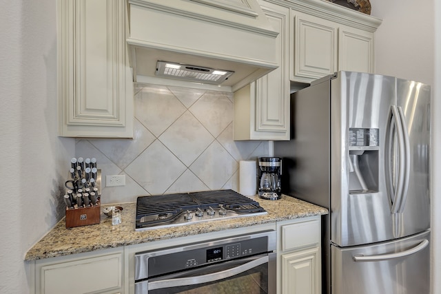 kitchen featuring light stone counters, appliances with stainless steel finishes, backsplash, and custom range hood