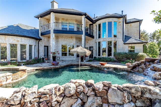 rear view of property with a balcony and a swimming pool with hot tub