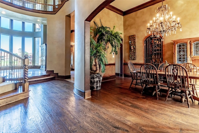 dining space with hardwood / wood-style floors, a towering ceiling, a notable chandelier, and ornamental molding