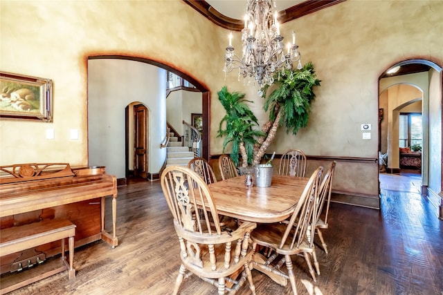 dining space with ornamental molding, a towering ceiling, hardwood / wood-style floors, and an inviting chandelier