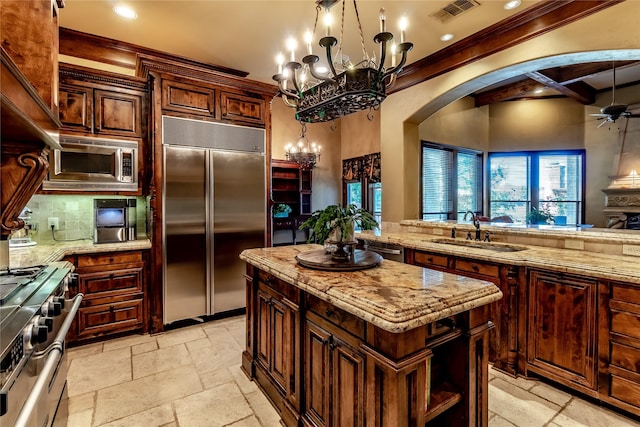 kitchen with sink, beam ceiling, ceiling fan with notable chandelier, a kitchen island, and built in appliances