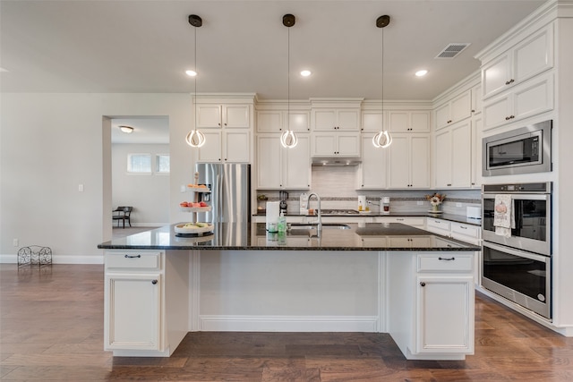 kitchen featuring appliances with stainless steel finishes, dark stone counters, a kitchen island with sink, dark hardwood / wood-style floors, and sink