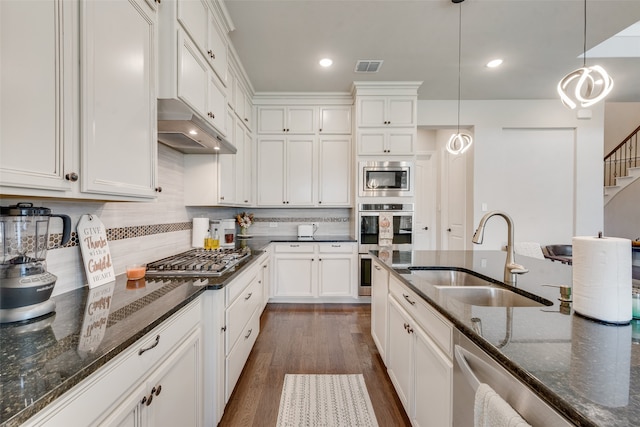 kitchen with dark stone countertops, white cabinetry, dark wood-type flooring, decorative light fixtures, and sink