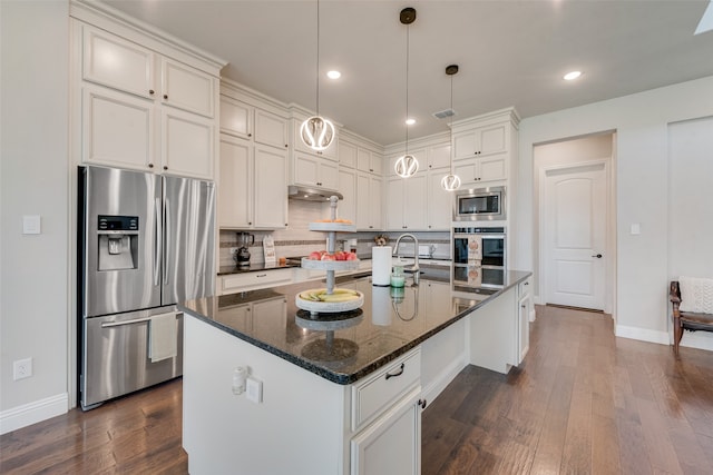 kitchen with a center island with sink, stainless steel appliances, dark hardwood / wood-style floors, and dark stone counters