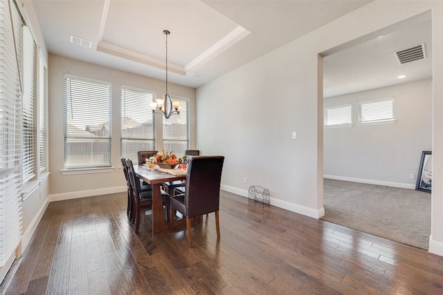 dining area with an inviting chandelier, a raised ceiling, dark hardwood / wood-style flooring, and a wealth of natural light