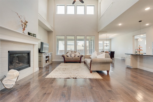 living room featuring wood-type flooring, ceiling fan with notable chandelier, and a tiled fireplace