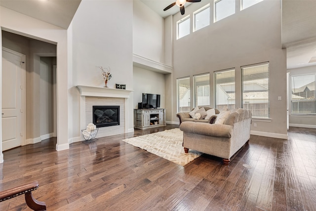 living room with ceiling fan, a towering ceiling, and dark wood-type flooring