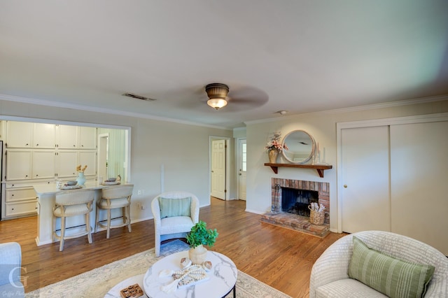 living room with a brick fireplace, light hardwood / wood-style flooring, ceiling fan, and ornamental molding