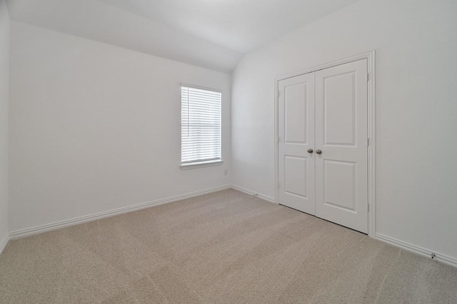 unfurnished bedroom featuring vaulted ceiling, light colored carpet, and a closet