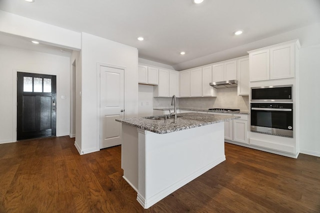 kitchen with sink, a kitchen island with sink, white cabinetry, stainless steel appliances, and light stone countertops