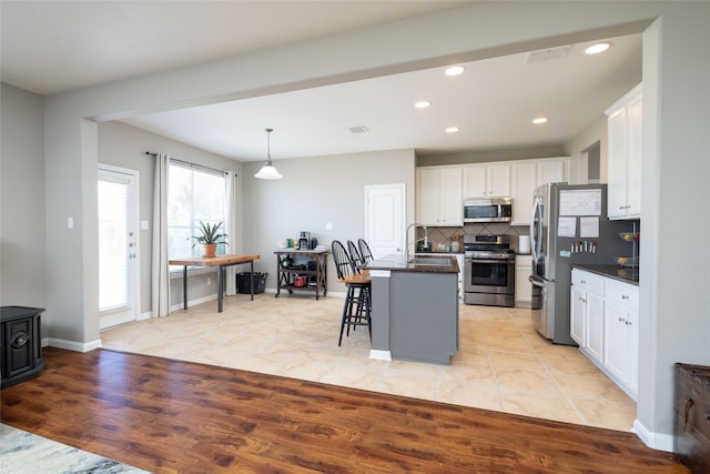 kitchen featuring appliances with stainless steel finishes, light wood-type flooring, a breakfast bar, white cabinets, and an island with sink