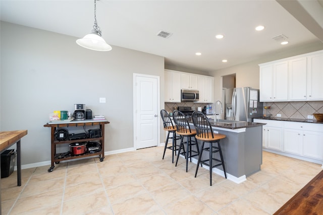 kitchen with a center island with sink, tasteful backsplash, a kitchen bar, white cabinetry, and stainless steel appliances