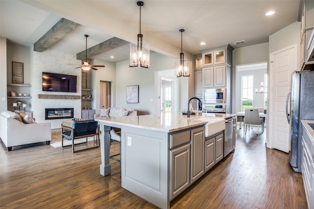 kitchen featuring light stone counters, a center island with sink, plenty of natural light, and beam ceiling