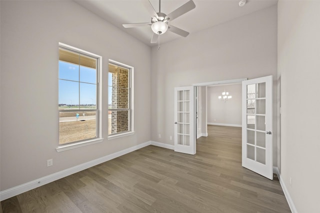 empty room featuring ceiling fan with notable chandelier, baseboards, wood finished floors, and french doors