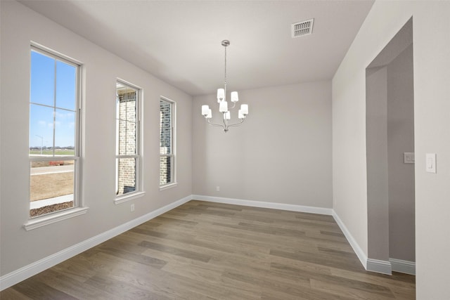 unfurnished dining area with a chandelier, visible vents, baseboards, and wood finished floors