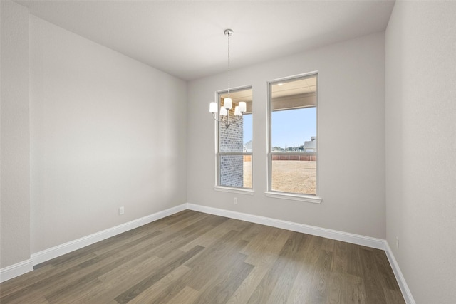 spare room with a chandelier, dark wood finished floors, and baseboards