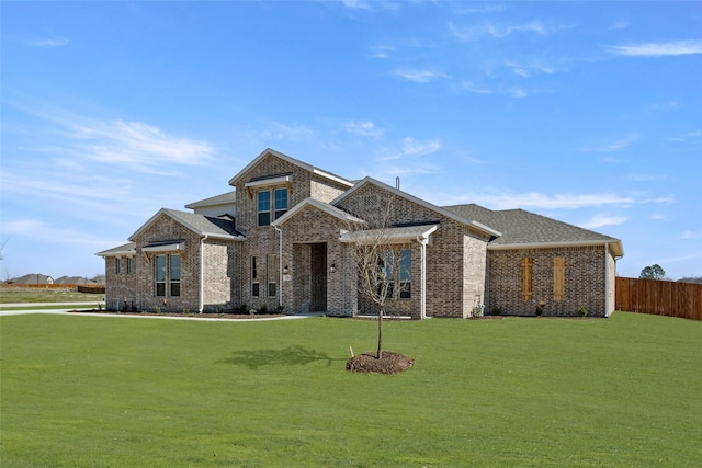 view of front of house featuring a front lawn, a shingled roof, fence, and brick siding