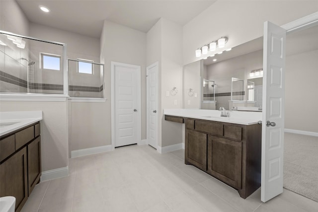 full bathroom featuring a sink, a stall shower, baseboards, and two vanities