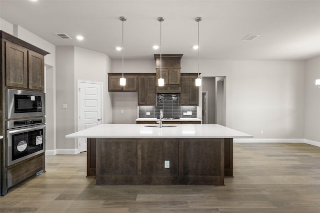 kitchen featuring tasteful backsplash, visible vents, stainless steel oven, a sink, and dark brown cabinets