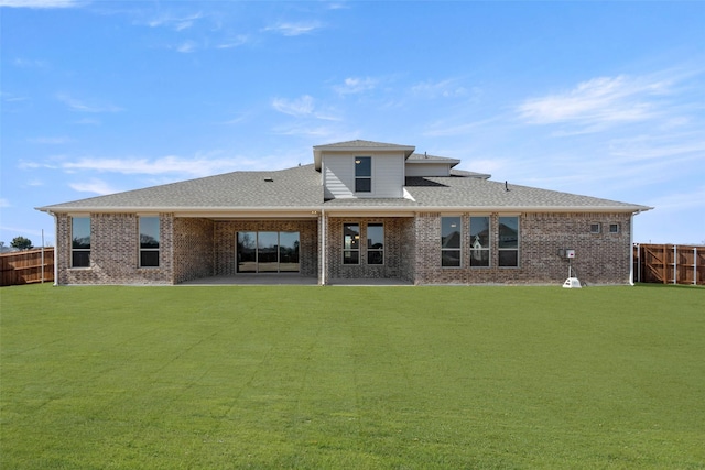 rear view of house with brick siding, a yard, a patio, a shingled roof, and fence