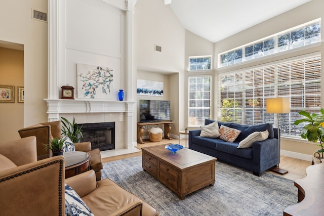 living room featuring high vaulted ceiling, a healthy amount of sunlight, a fireplace, and light hardwood / wood-style flooring