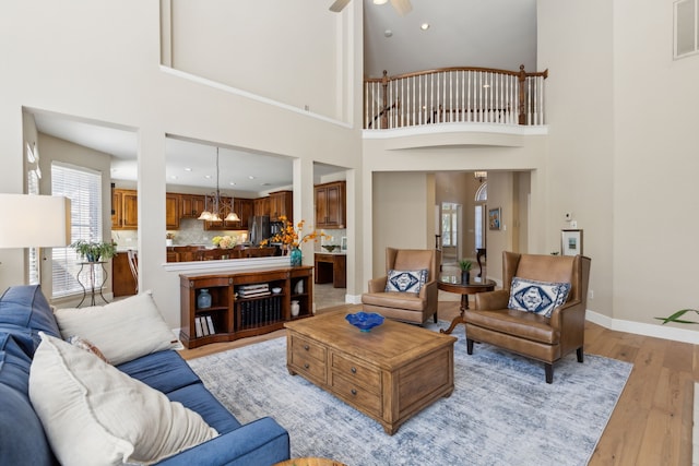 living room featuring a high ceiling, ceiling fan, and light hardwood / wood-style flooring