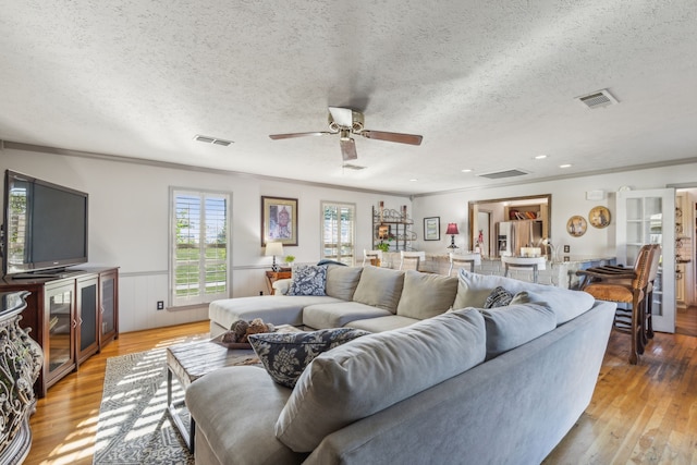 living room featuring light hardwood / wood-style flooring, a textured ceiling, ceiling fan, and crown molding