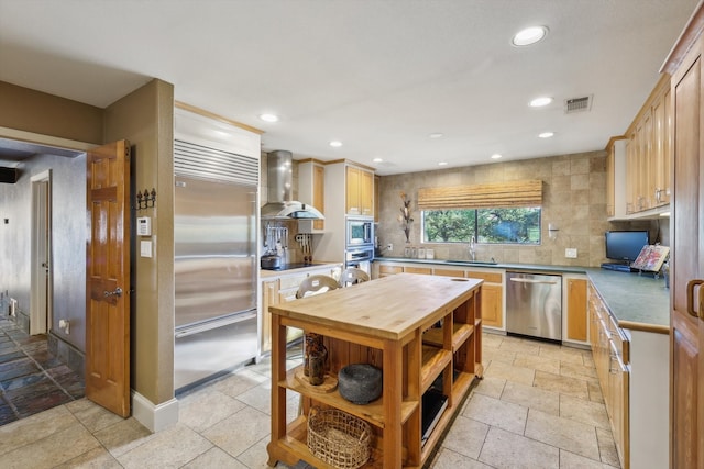 kitchen with wall chimney exhaust hood, light brown cabinetry, and built in appliances