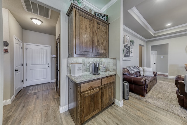 kitchen with backsplash, ornamental molding, light hardwood / wood-style flooring, and light stone counters