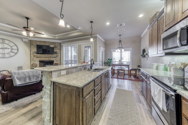 kitchen featuring an island with sink, appliances with stainless steel finishes, hanging light fixtures, and a fireplace