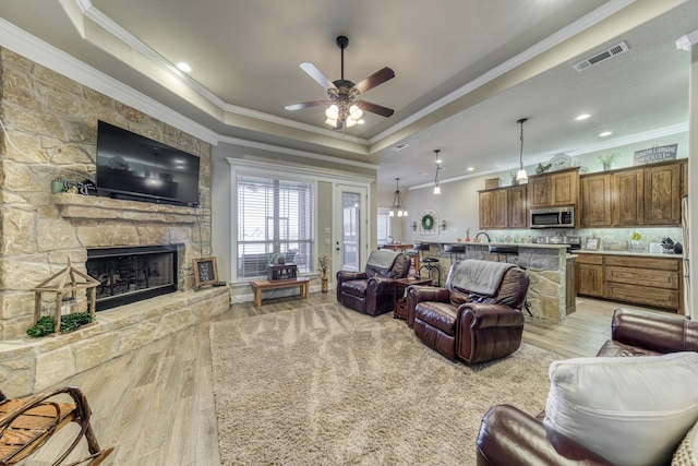 living room featuring a stone fireplace, crown molding, light hardwood / wood-style floors, and a tray ceiling