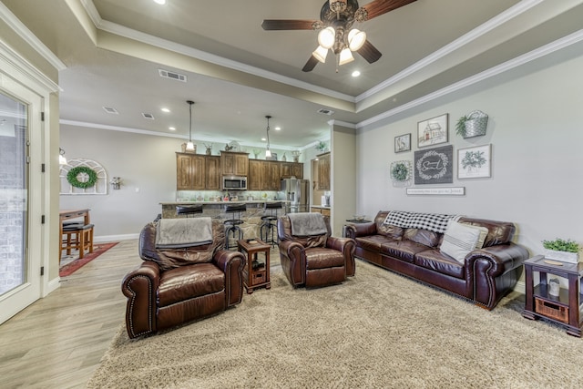 living room featuring crown molding, light hardwood / wood-style floors, ceiling fan, and a raised ceiling