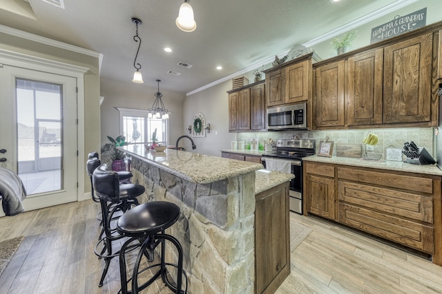 kitchen featuring pendant lighting, a kitchen island with sink, backsplash, stainless steel appliances, and light hardwood / wood-style floors