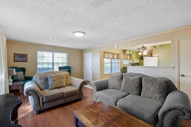 living room with wood-type flooring, a textured ceiling, ceiling fan, and crown molding