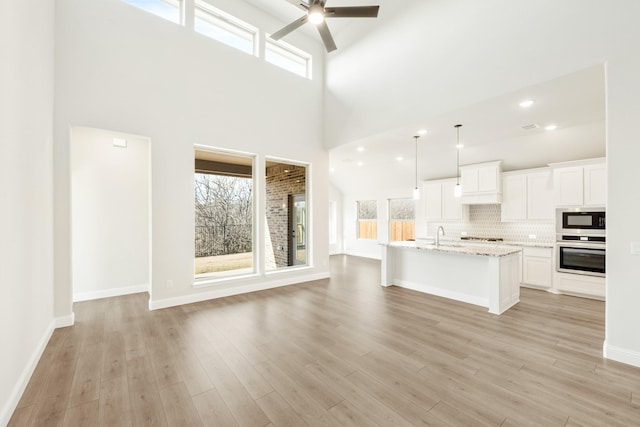 unfurnished living room with light hardwood / wood-style floors, ceiling fan, and high vaulted ceiling