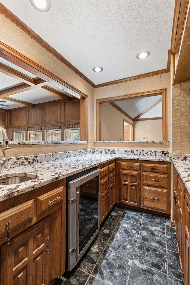 kitchen with light stone countertops, a textured ceiling, beverage cooler, crown molding, and sink