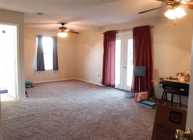 unfurnished living room with a textured ceiling, ceiling fan, carpet floors, visible vents, and baseboards