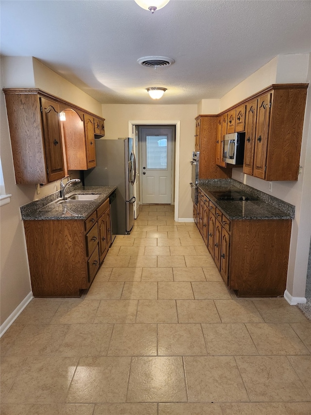 kitchen featuring stainless steel appliances, dark stone countertops, sink, and a textured ceiling