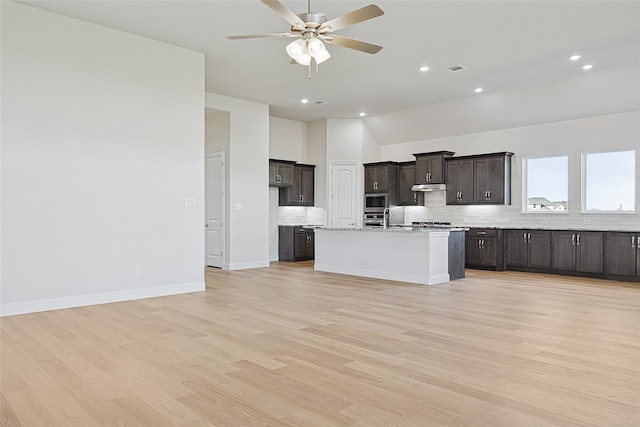 kitchen featuring ceiling fan, stainless steel microwave, backsplash, light hardwood / wood-style floors, and a kitchen island with sink