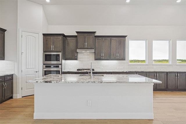 kitchen featuring backsplash, stainless steel appliances, a kitchen island with sink, and light hardwood / wood-style flooring