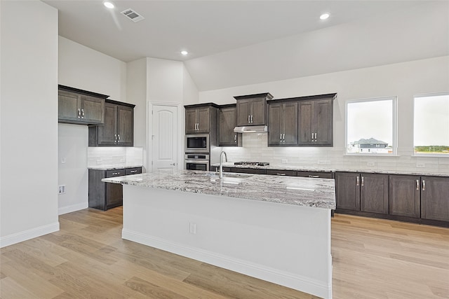 kitchen with sink, stainless steel appliances, light hardwood / wood-style flooring, vaulted ceiling, and a center island with sink