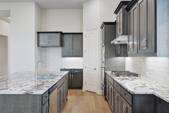 kitchen with sink, light hardwood / wood-style flooring, decorative backsplash, light stone counters, and stainless steel appliances