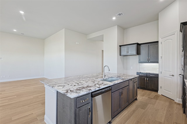 kitchen featuring sink, light stone counters, light hardwood / wood-style flooring, stainless steel dishwasher, and an island with sink