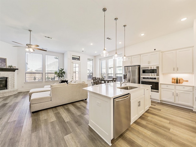 kitchen with white cabinetry, stainless steel appliances, an island with sink, and hanging light fixtures