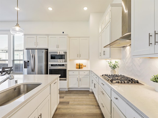 kitchen featuring wall chimney exhaust hood, decorative light fixtures, stainless steel appliances, decorative backsplash, and sink