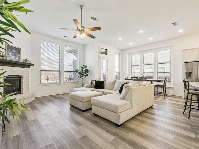 living room featuring a brick fireplace, a wealth of natural light, light hardwood / wood-style flooring, and ceiling fan