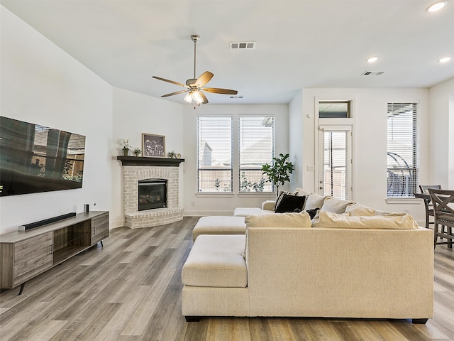 living room featuring a brick fireplace, ceiling fan, and light wood-type flooring