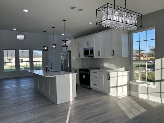 kitchen with appliances with stainless steel finishes, a notable chandelier, a sink, wood finished floors, and visible vents