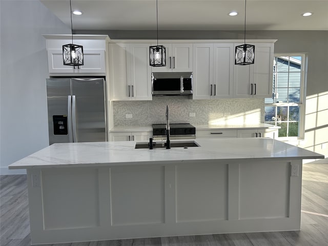 kitchen featuring wood-type flooring, hanging light fixtures, stainless steel appliances, white cabinets, and a kitchen island with sink