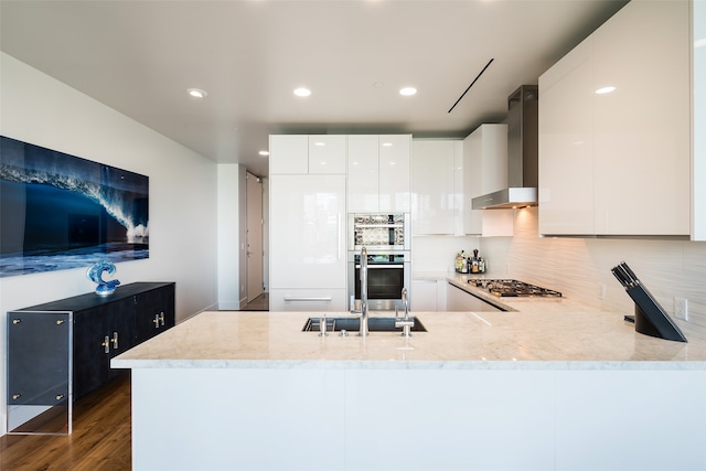 kitchen featuring dark wood-type flooring, white cabinetry, kitchen peninsula, wall chimney range hood, and stainless steel appliances